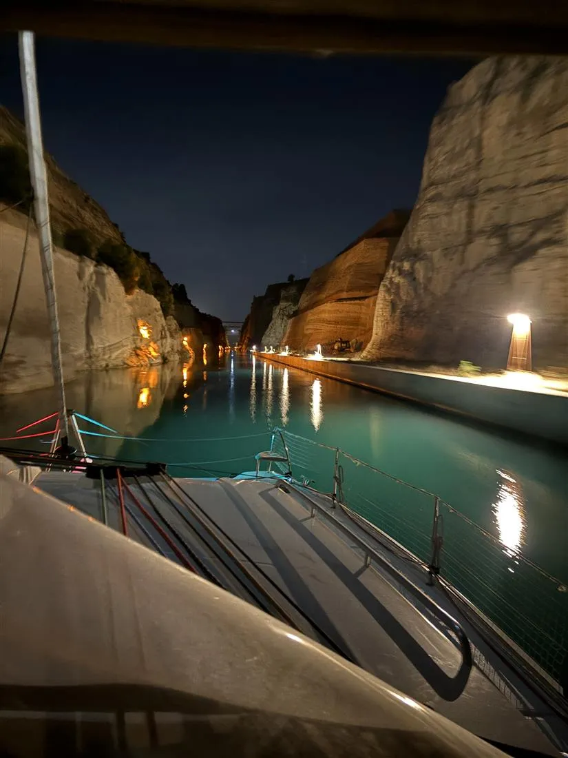 A catamaran passing through the Corinth Canal at night, cliffs lit on both sides