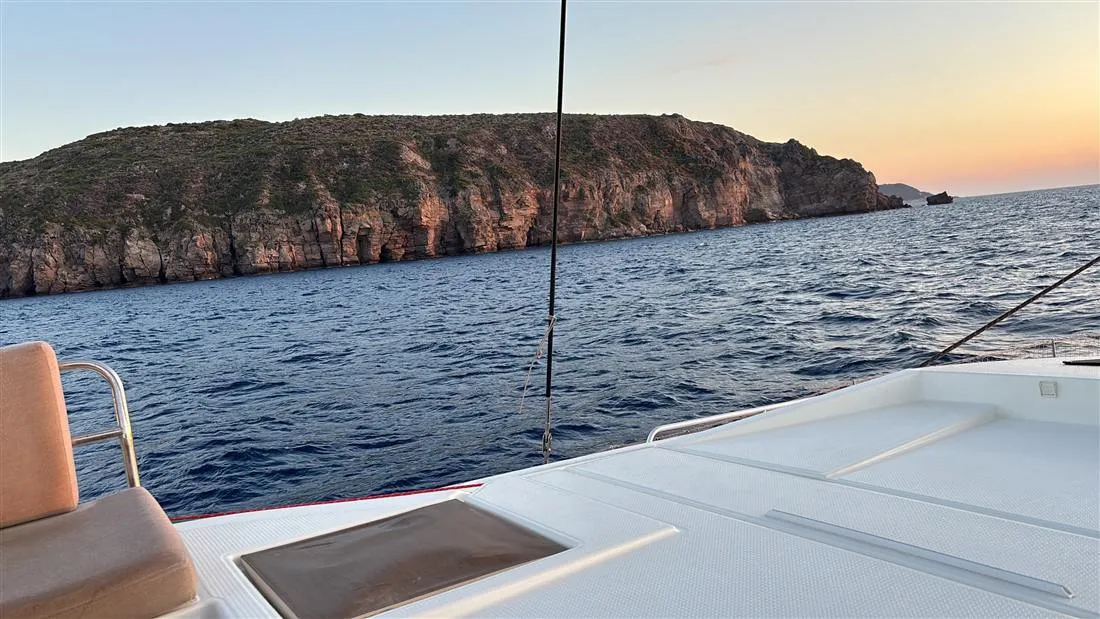 View from a catamaran deck towards red cliffs at sunset