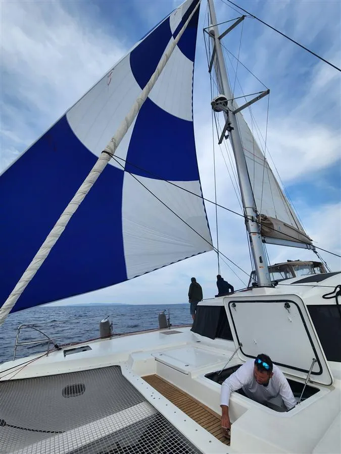 Shai at work in a deck hatch under a blue and white spinnaker