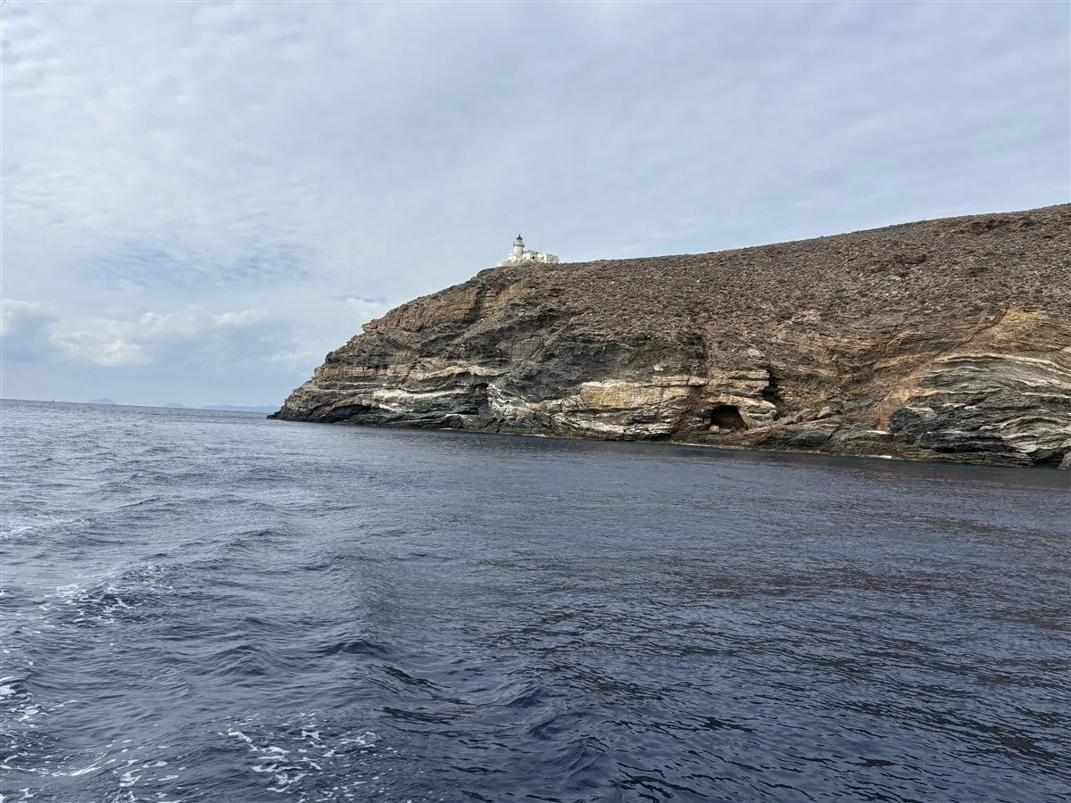 A lighthouse on a rocky Greek headland seen from the water
